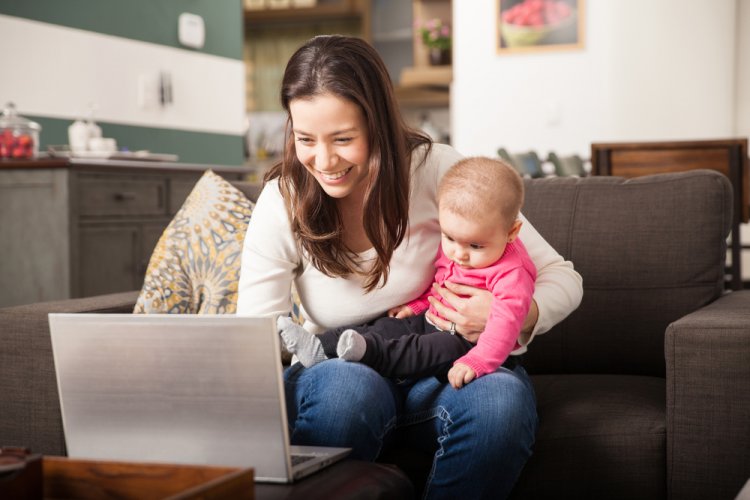 woman in her home looking at laptop holding a baby