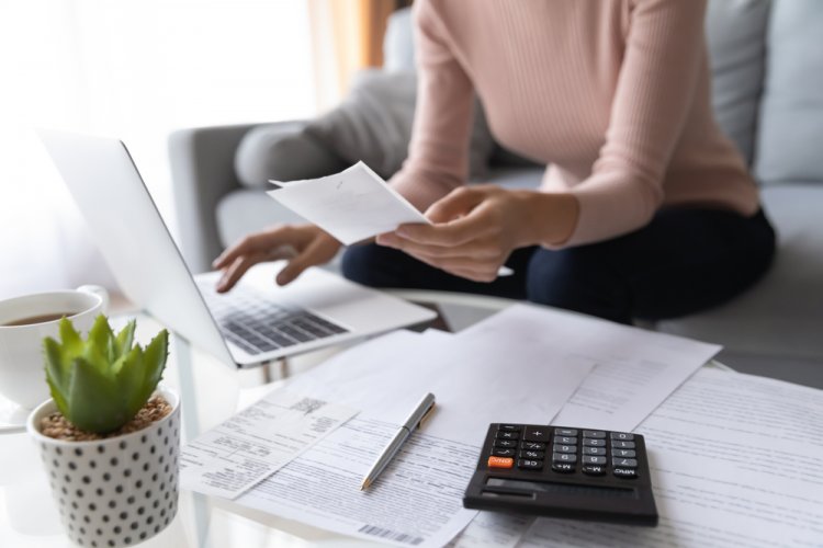 woman on living room with calculator looking at car papers