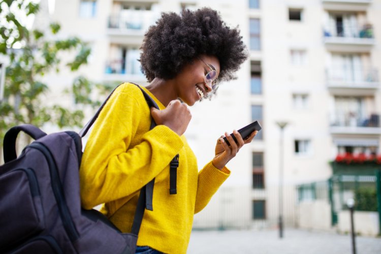 Sideview of smiling african woman walking in city with bag and phone