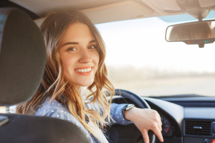 smiling young female driver at the wheel of a car wondering if she needs car insurance