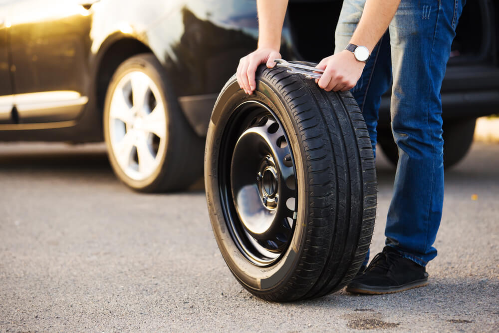 man holding an emergency spare tire with a car in the background