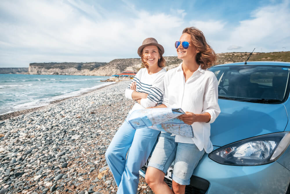 two women in car smiling and looking at map near the ocean