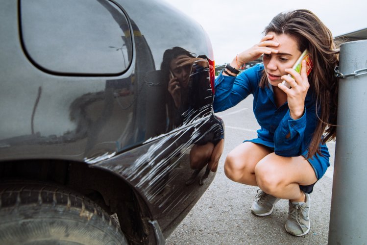 worried woman talking on phone next to damaged car