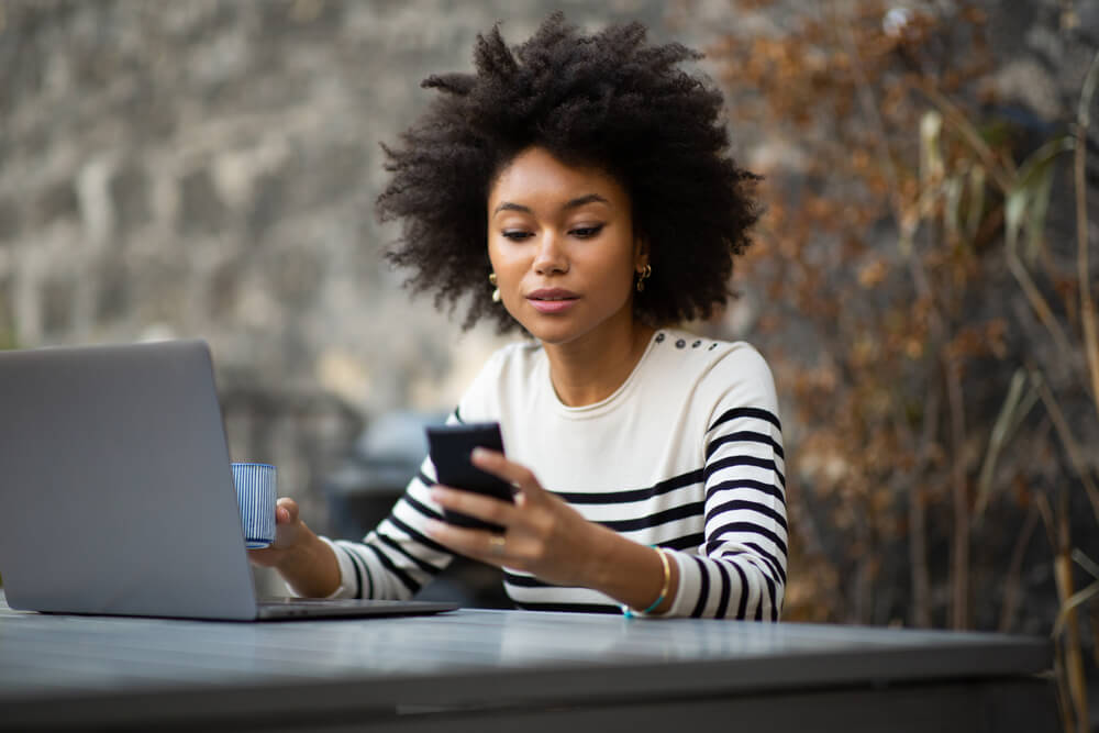 young african american woman sitting with laptop and using mobile phone