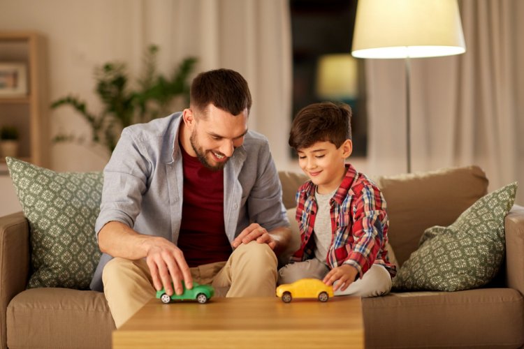 happy father and son playing with toy cars at home