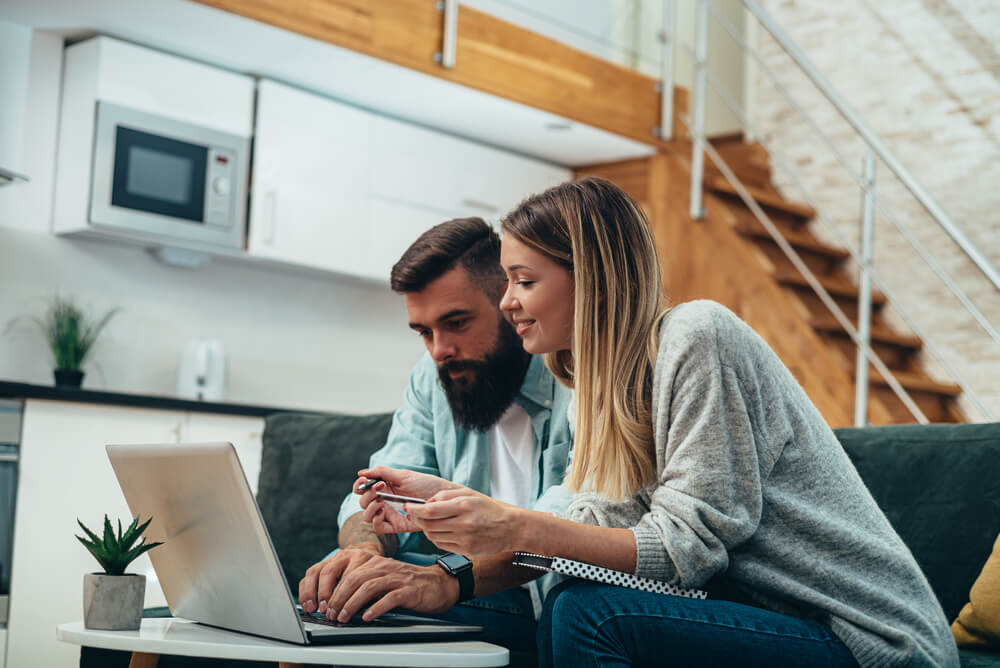 Shot of a young couple using a credit card and laptop for finding car insurance discounts