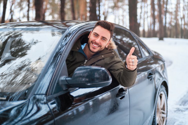young man leaning out of car window with thumbs up in winter