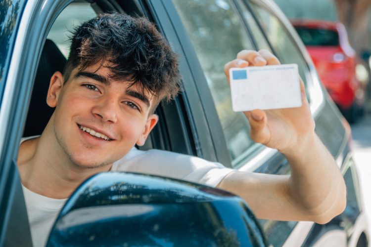 Young driver proudly displays his license while sitting behind the wheel