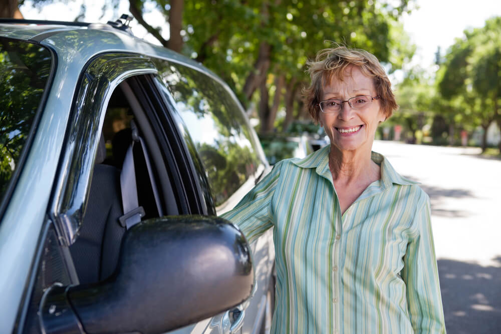 senior citizen woman smiling standing outside of car