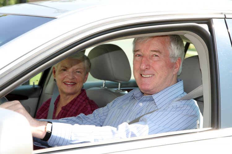 senior citizen man and wife smiling in front seats of car
