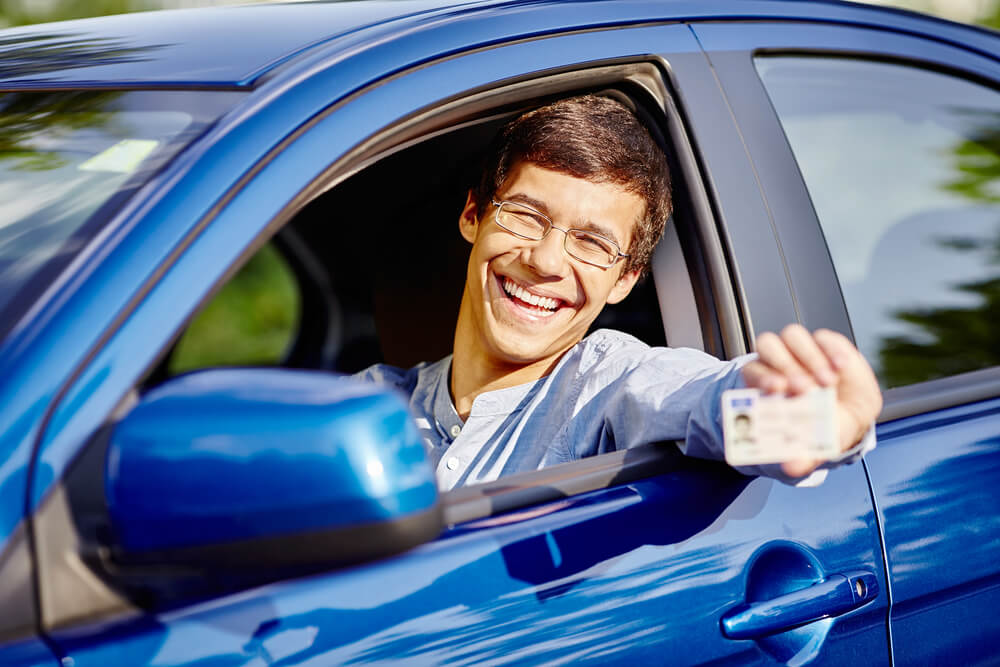 young teenage boy in car showing off drivers license while smiling
