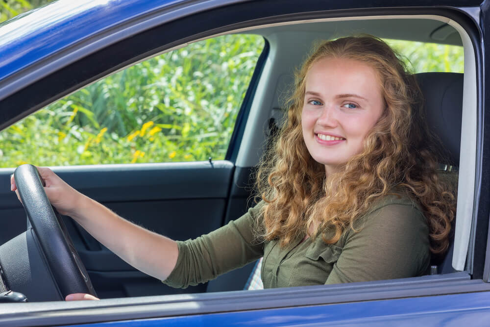 young teenage girl in driver's seat of car smiling