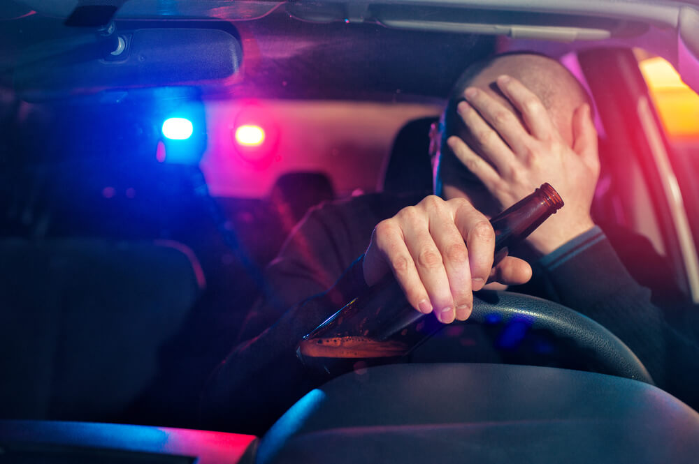 man driving getting pulled over with beer bottle in hand