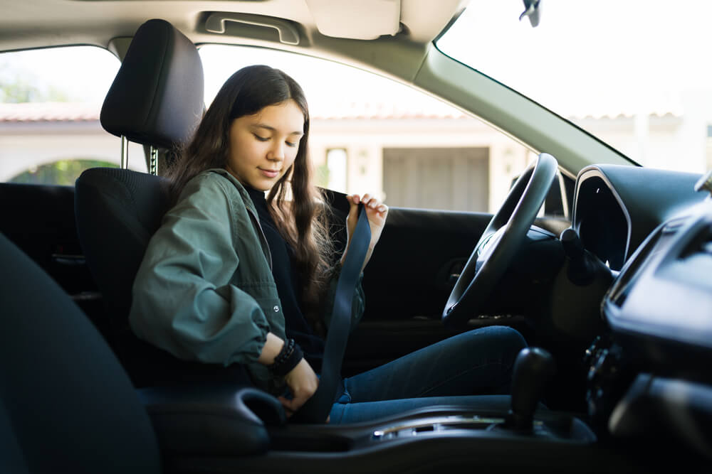 young teenage girl putting on her seat belt in drivers seat of car