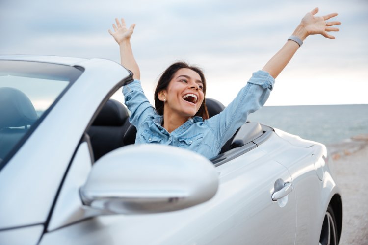 young woman in convertible with hands in the air