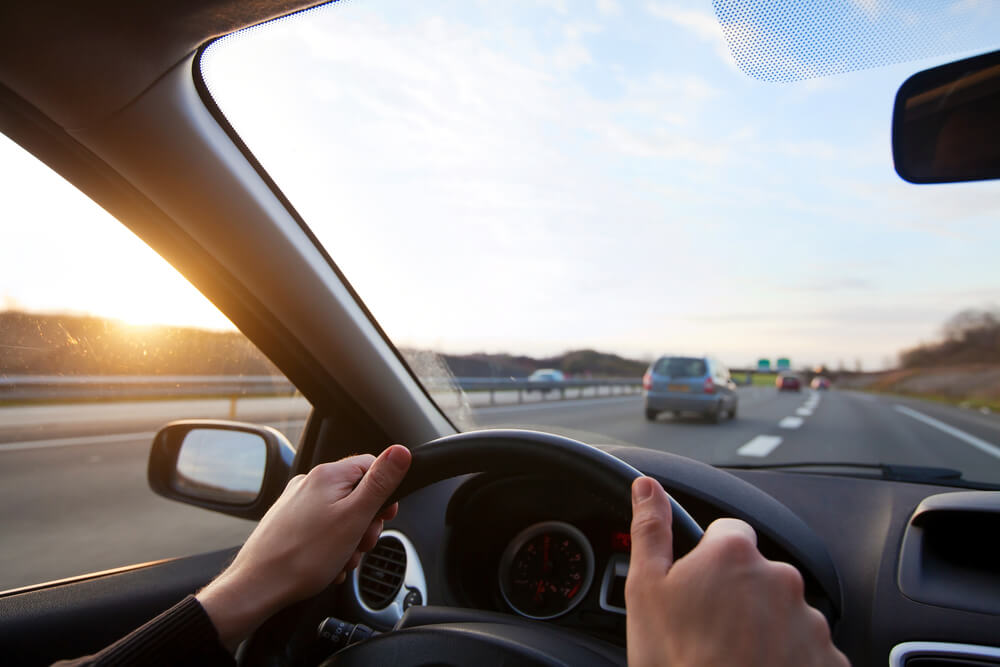 person with hands on the wheel of a car driving down highway