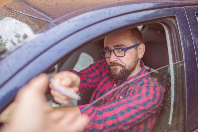 caucasian man in driver's seat of car handing over license