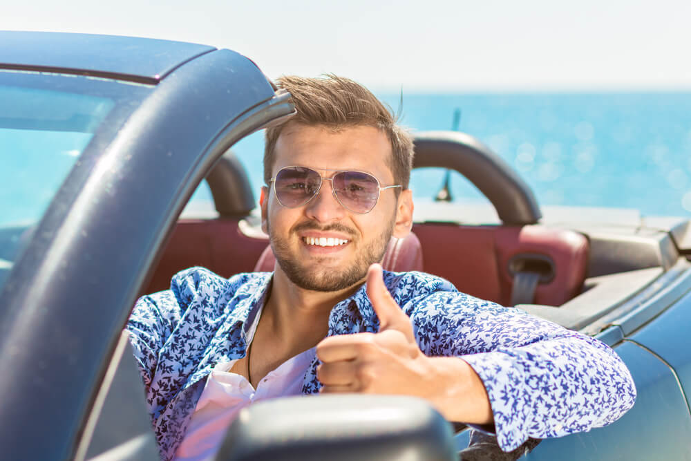 Young man driving a sports car and flashing a thumbs up