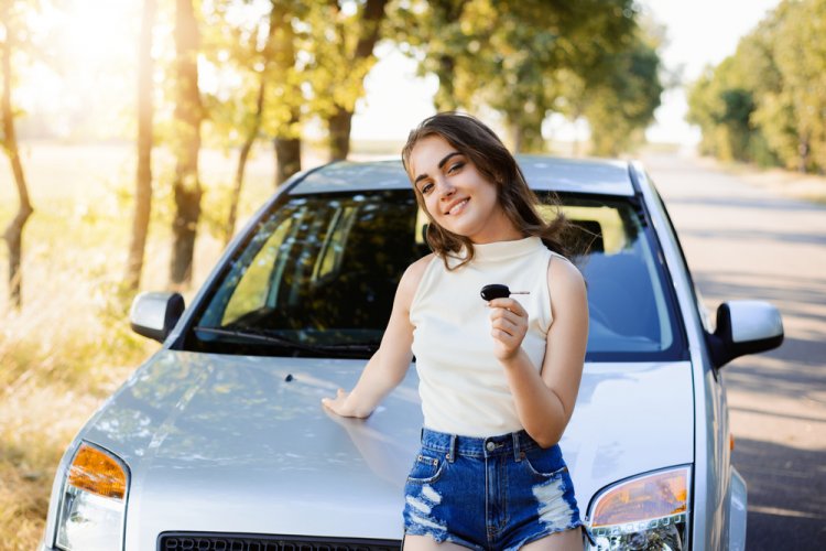 Young driver holds key to a car in the background