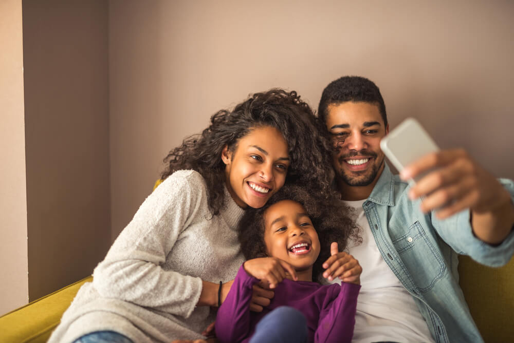 African American couple with young daughter smiling and taking a selfie while buying life insurance