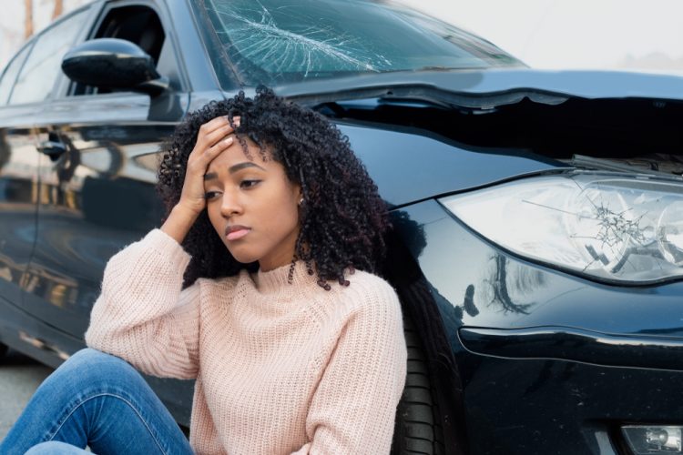 woman sitting outside of vehicle after accident holding her head