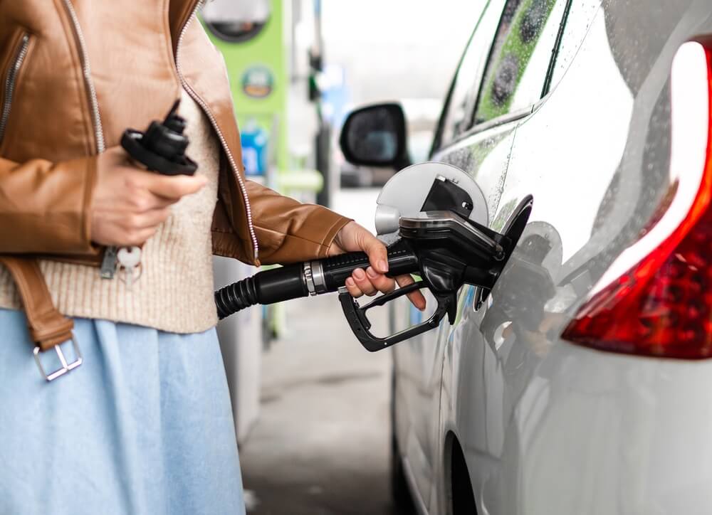 Woman fueling her car at a gas station while following tips to save gas mileage.