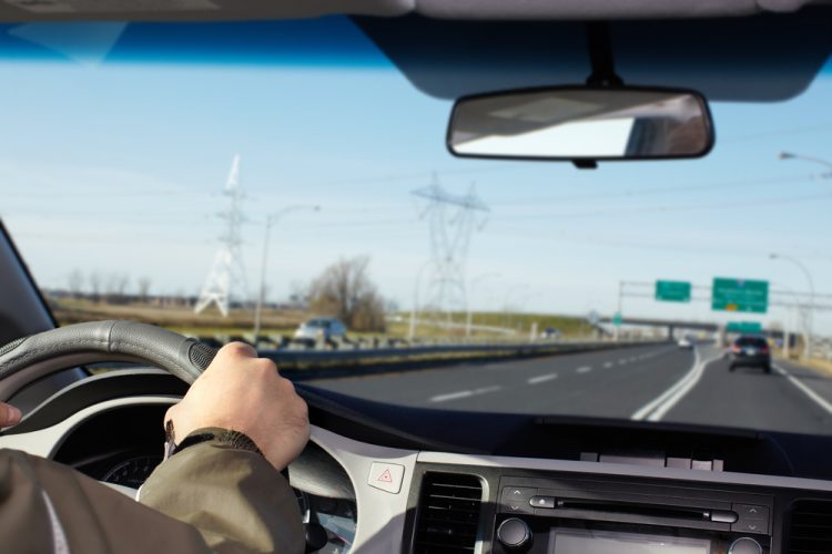 person with hand on wheel of car driving down highway