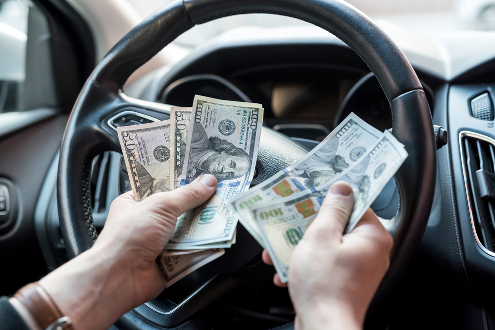 A man behind the wheel counts his cash to see how much it will cost if he doesn't stay under lease mileage 