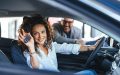 Curly-haired woman smiles from the driver’s seat and holds up a car key fob while a salesperson stands outside the open door, capturing a confident purchase and how to beat the car salesman.