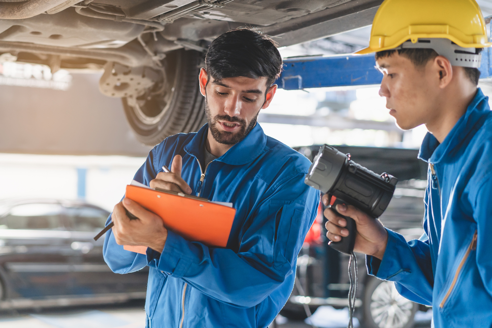 Two Hispanic mechanics look at car recall insurance instructions