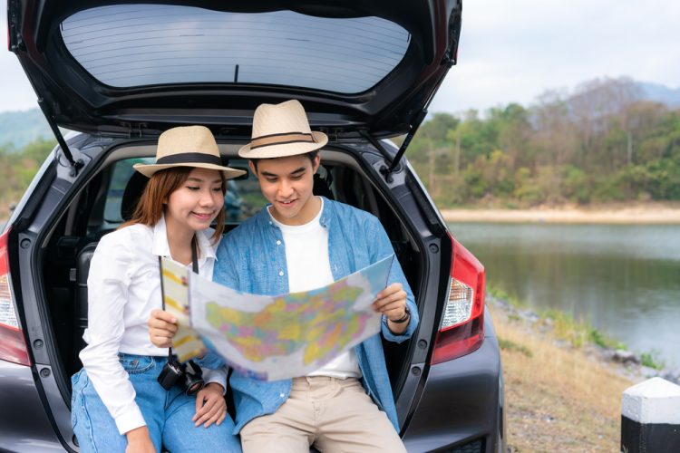 young asian couple looking at map sitting in back of car