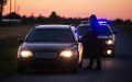 Police officer speaking to a driver during a traffic stop at sunset, requesting proof of car insurance.