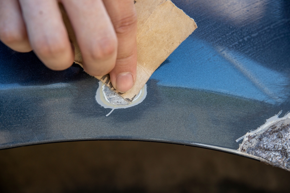 Hand using sandpaper to buff out car rust