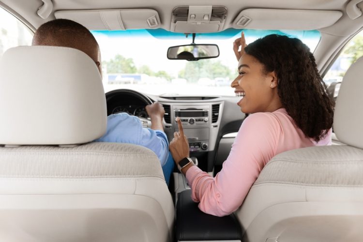 View from behind of black couple in car rocking out to music