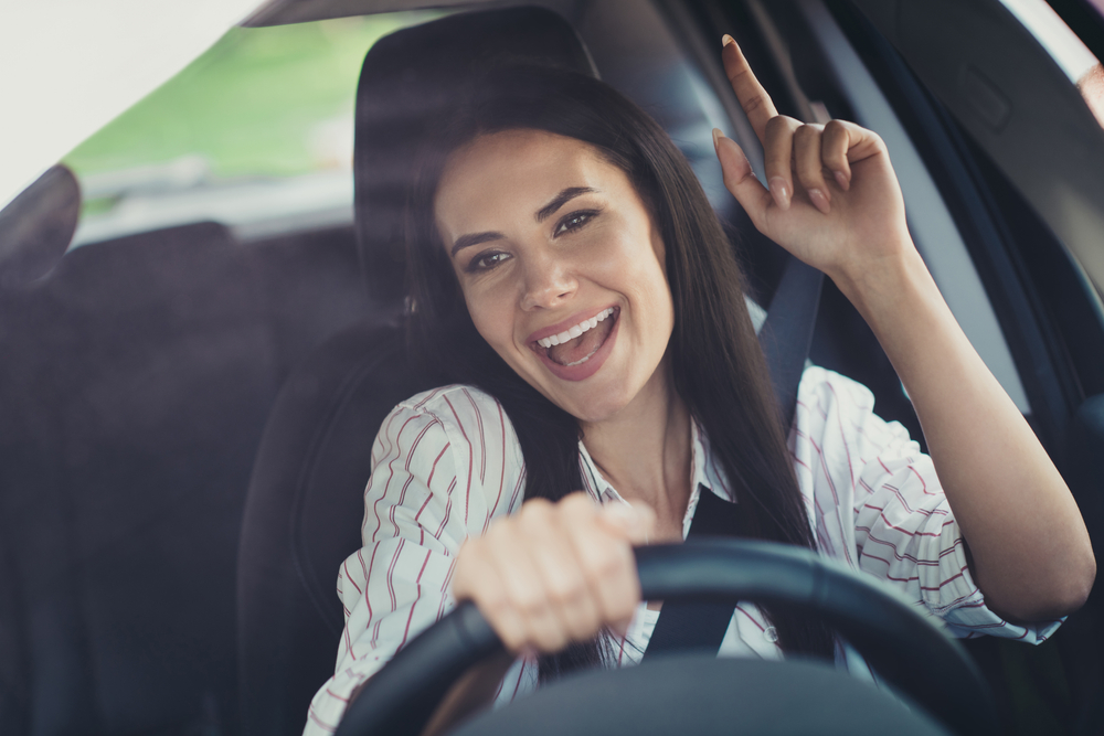 Happy attractive brunette rocking out to music in the front seat of her car