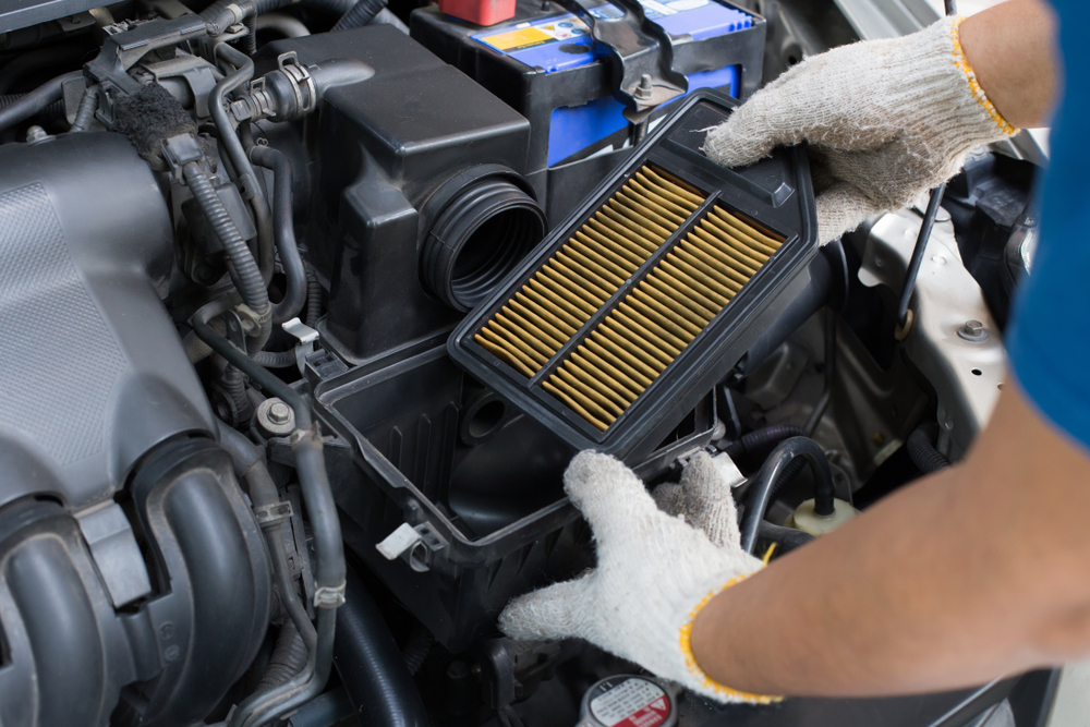 Mechanic hand holding an old and dirty car air filter to replace with a new filter.