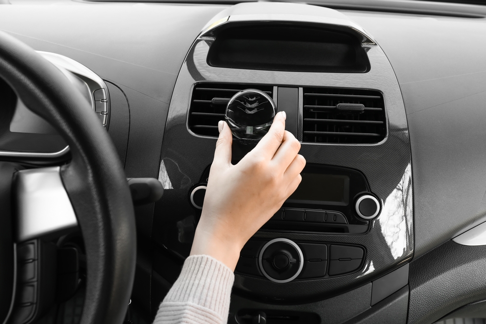 Hand positions a car air freshener on the air vent in the cabin