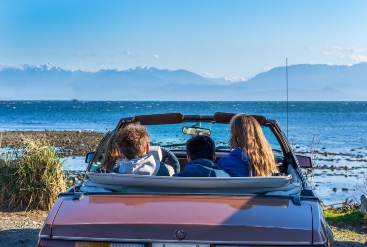 Convertible Car with young people sits facing the ocean