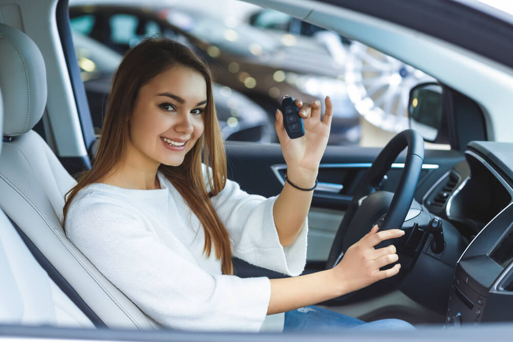 Teen driver holding car keys while sitting in a new vehicle, illustrating the best types of cars for your teen.
