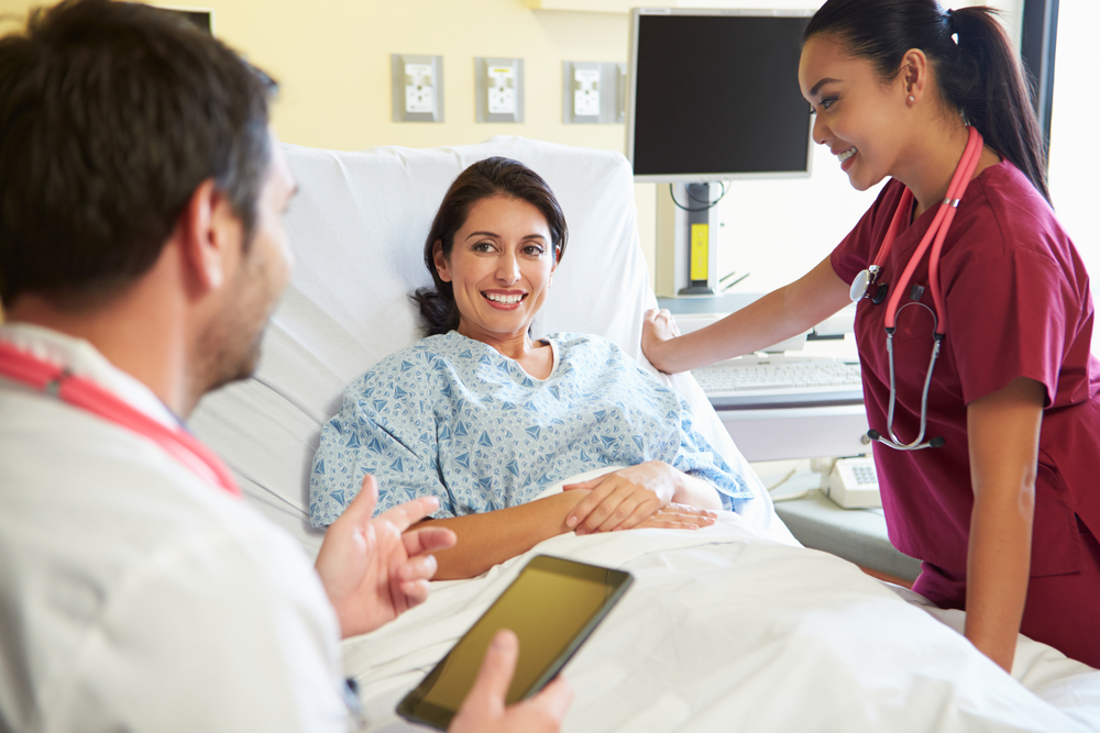 Hispanic woman in hospital bed consulting with doctor and African American nurse in scrubs