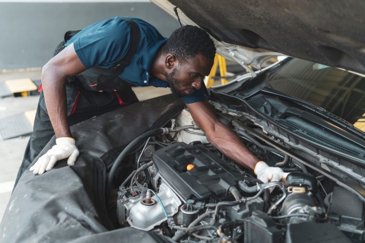 African-American car mechanic looks under the hood