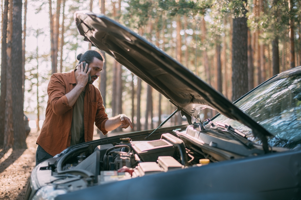 Man parked on side of road looking under the hood with car trouble