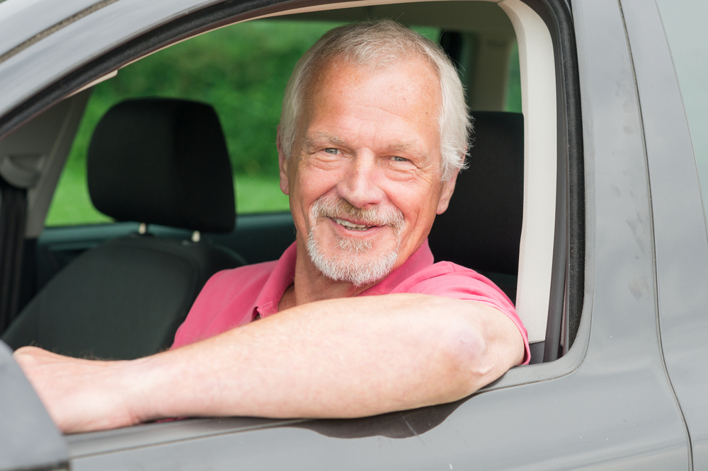 Senior man driving car smiling because car insurance savings - cheap car insurance