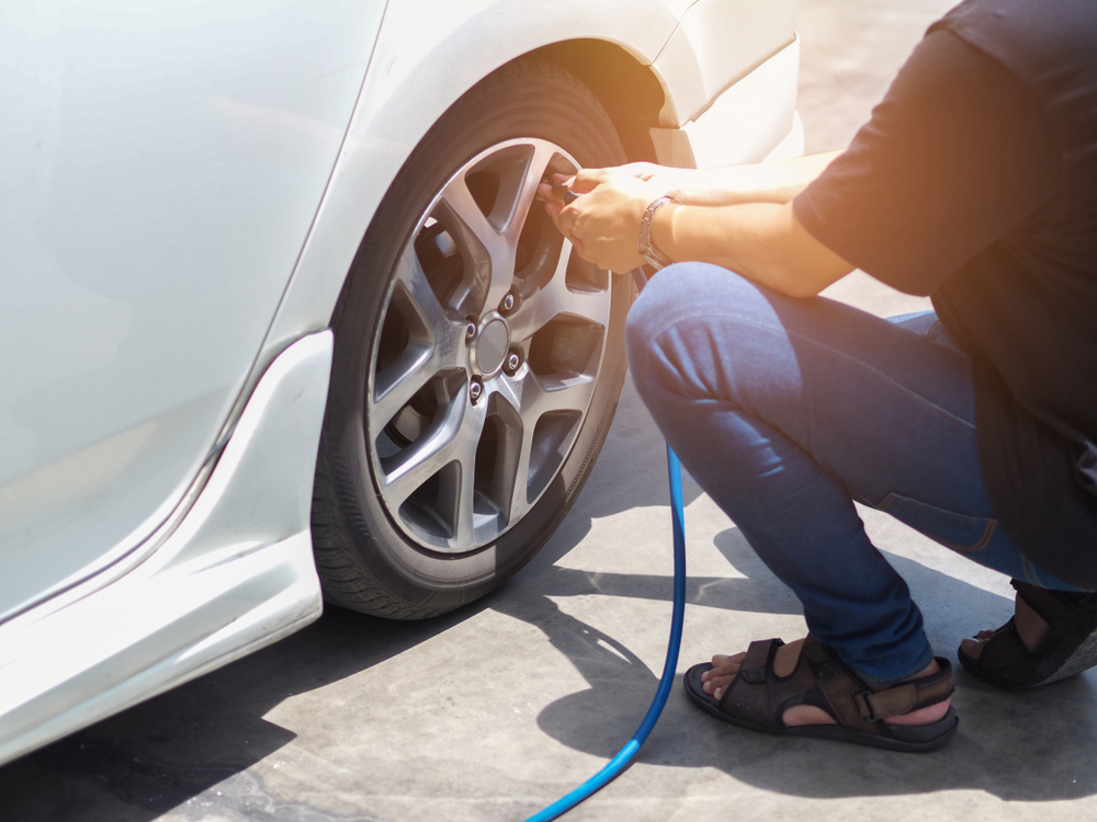 A man uses an air hose at the gas station to put air in his tire