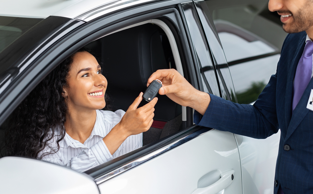 Smiling woman takes keys from car salesman as she sits in the front seat