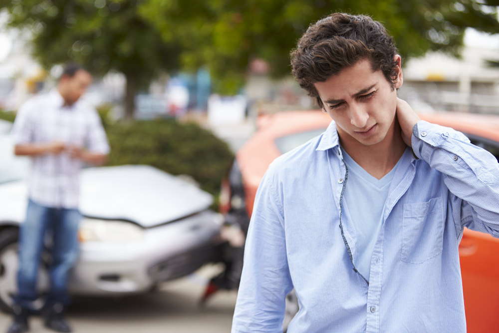 Teenager rubs his neck after getting rear-ended by an at-fault driver