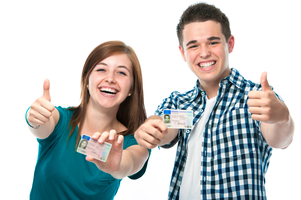 Two teens smiling proudly showing their new driver's license.