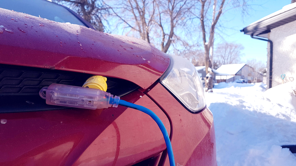 An engine block heater is plugged into a red car with snow on the ground