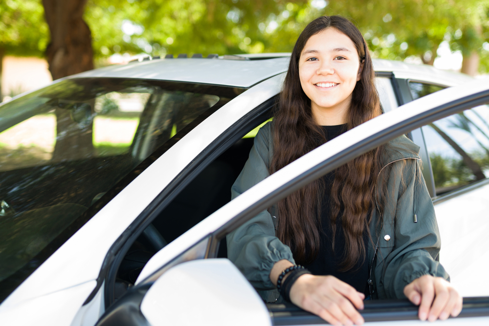 Teenage girl standing outside of driver's side of car.