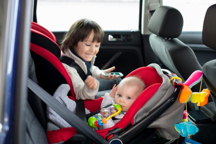 Older sibling in car seat looks over at younger sibling in car seat in back seat of car - car insurance in Louisiana